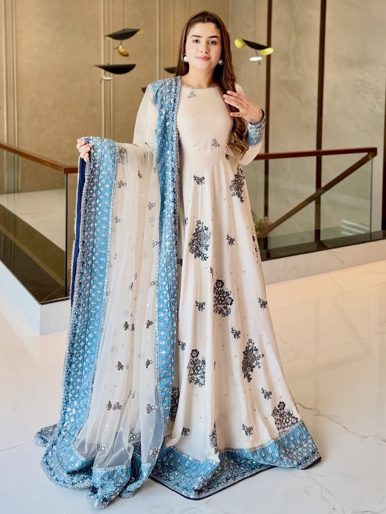 Woman in a white and blue traditional outfit standing in an indoor setting.