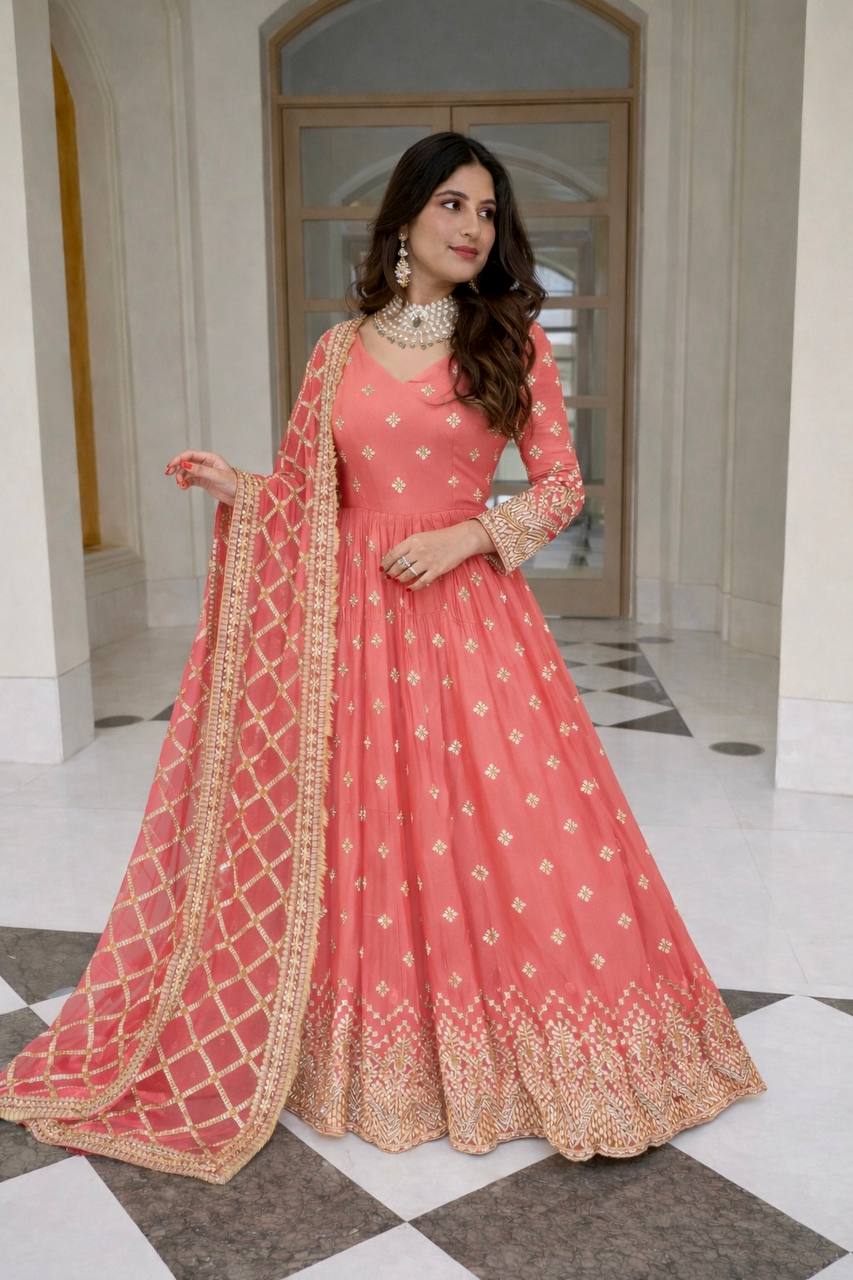 Woman in a pink traditional outfit with gold embroidery standing in an elegant interior setting.