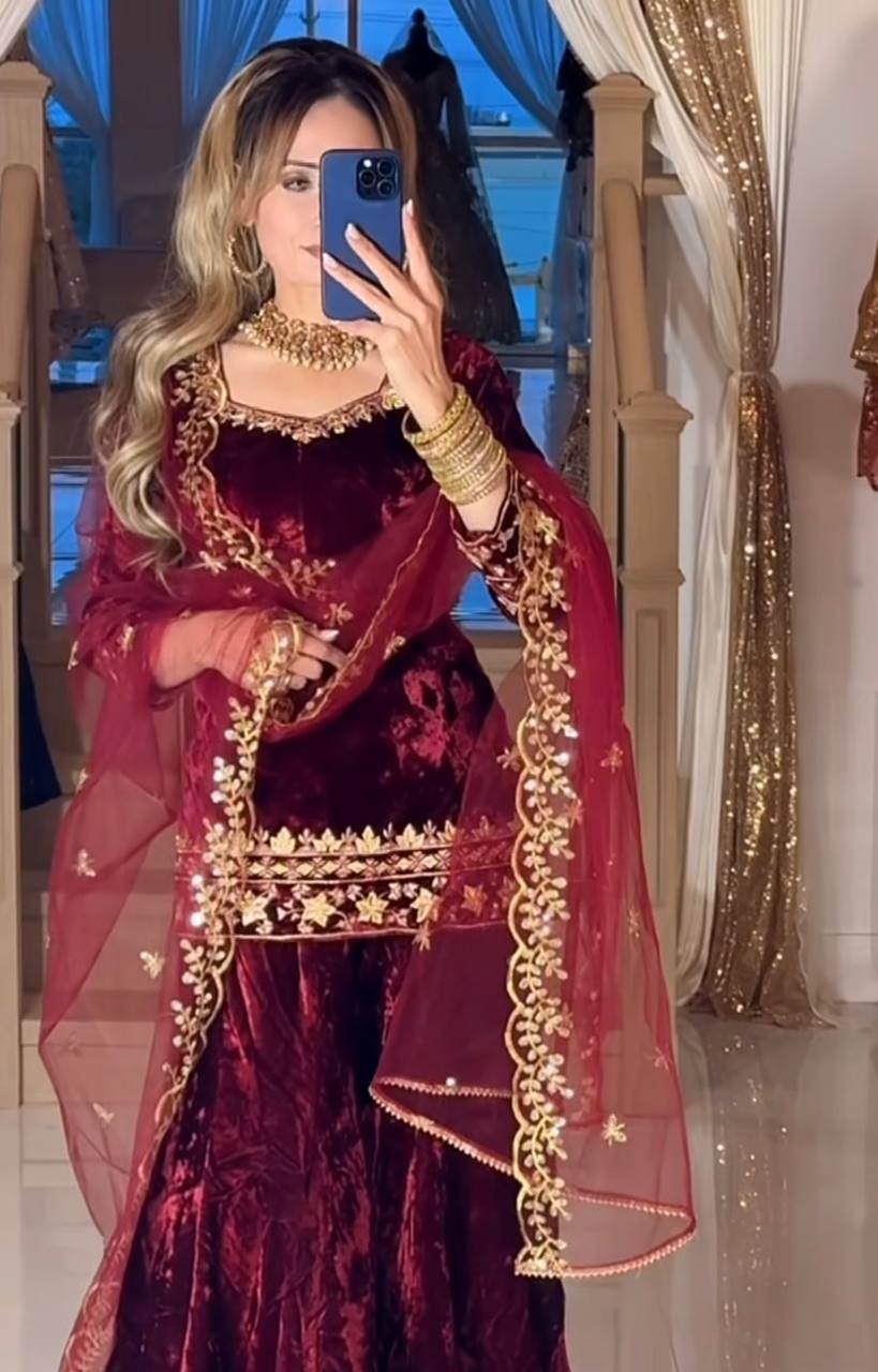 Woman in a maroon traditional outfit with gold embroidery taking a mirror selfie.