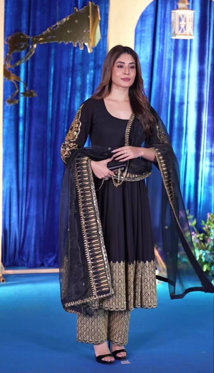 Woman in a black and gold traditional outfit against a blue curtain background