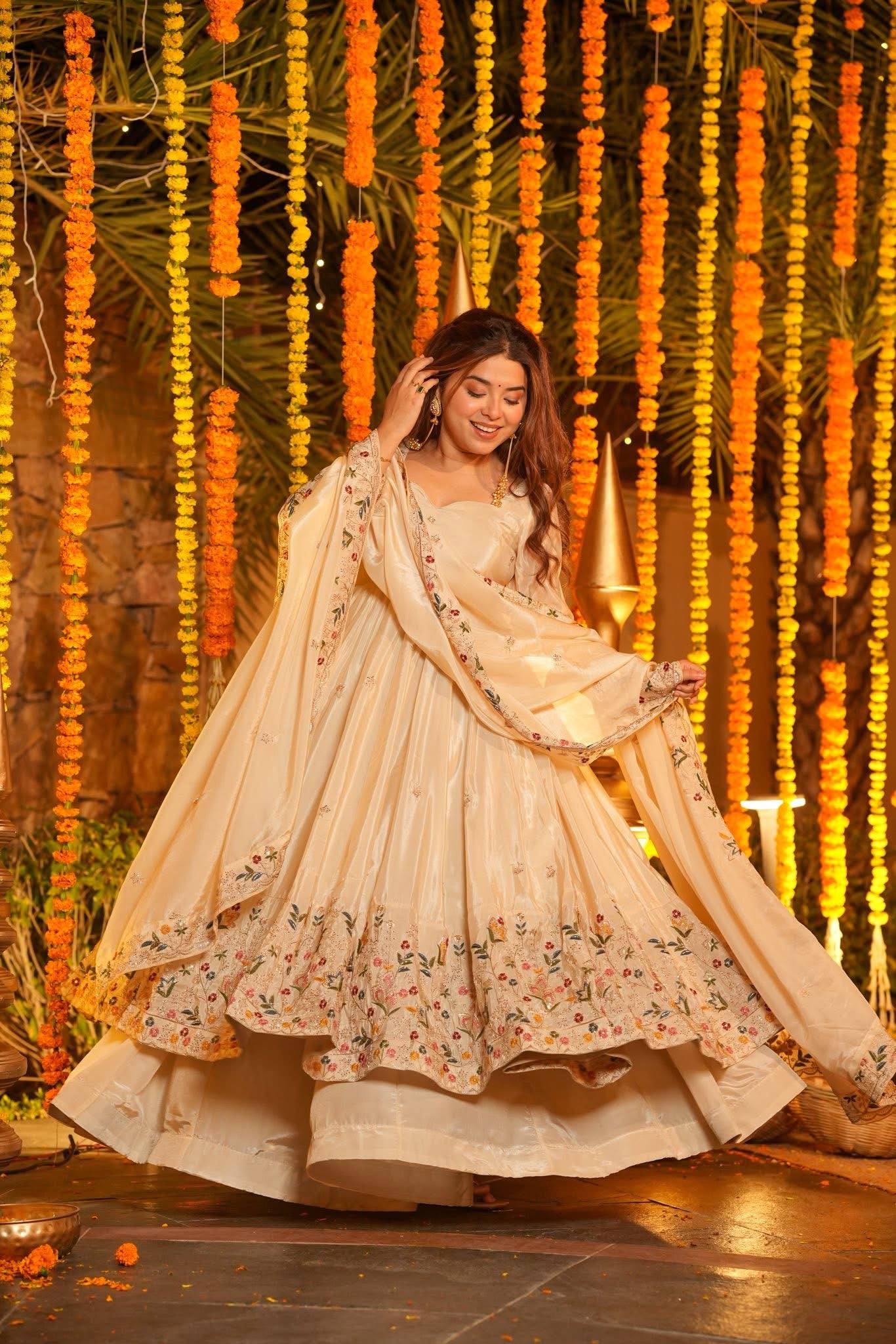 Woman in a traditional outfit with floral patterns against a decorative background with hanging flowers.
