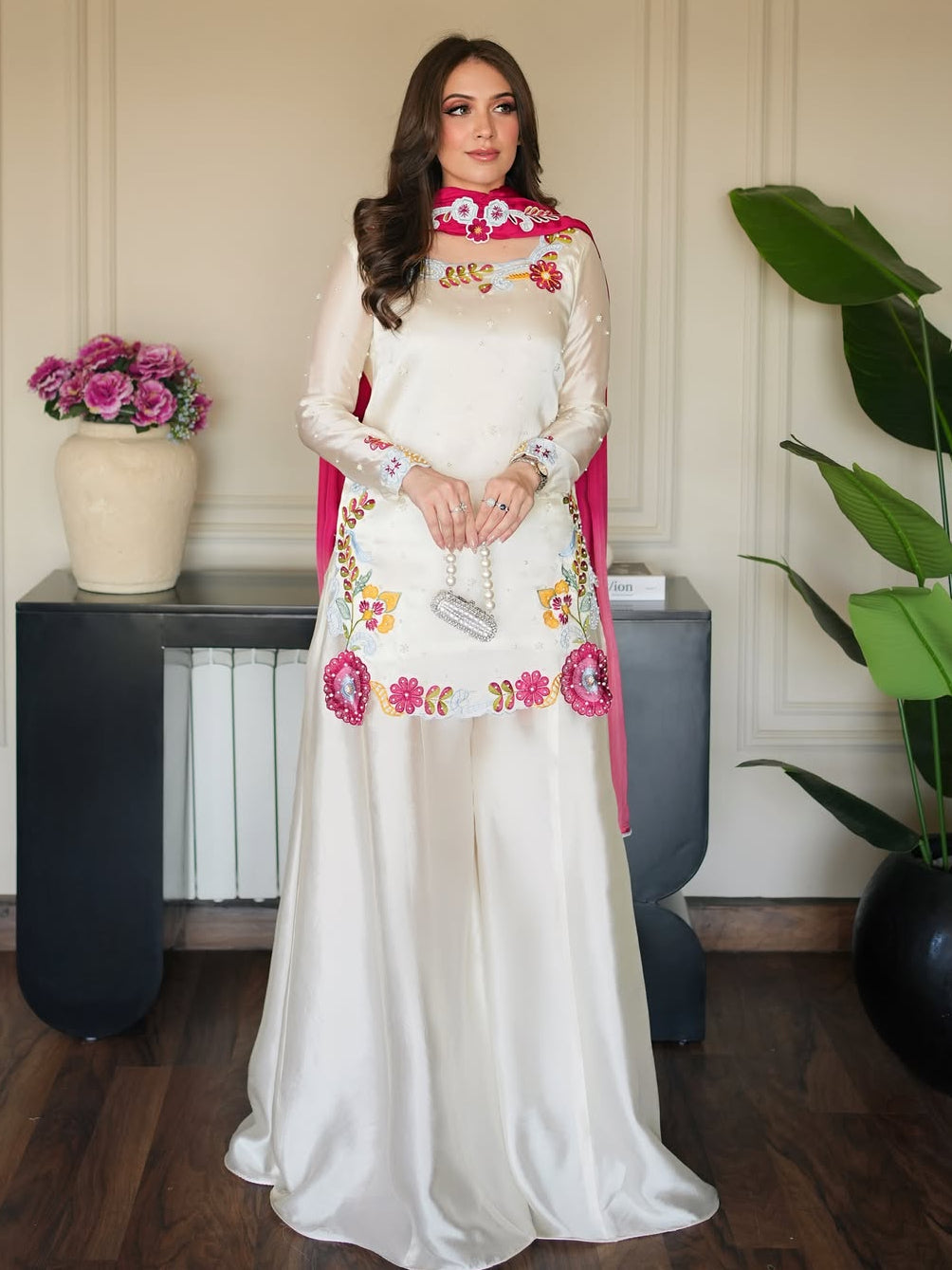 Woman in a white dress with floral embroidery standing indoors.