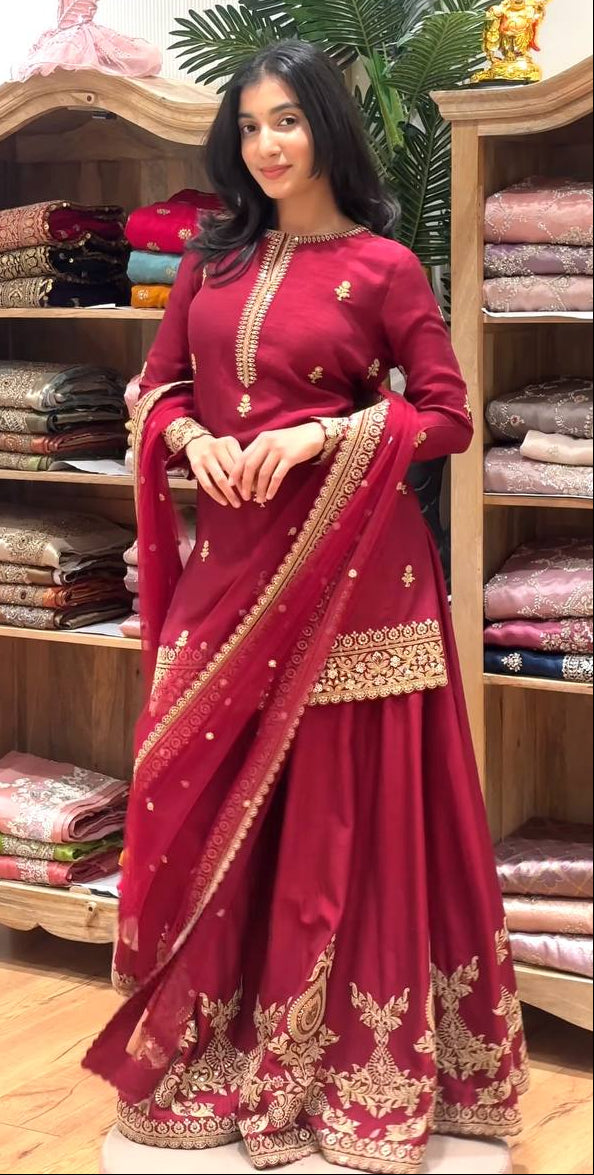 Woman in a red saree with gold embroidery standing in front of shelves displaying various fabrics.