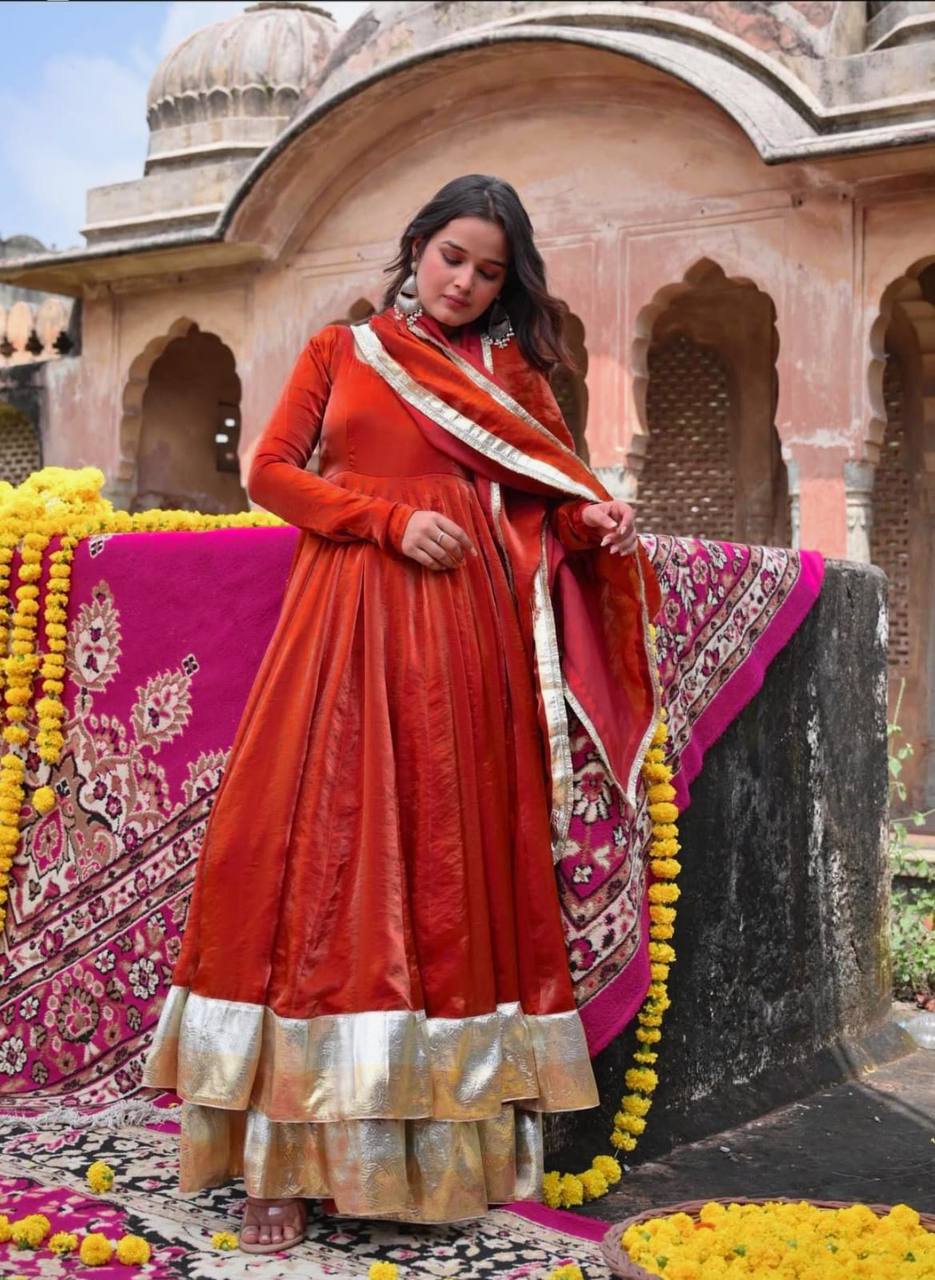 Woman in traditional red and gold outfit with a pink and yellow floral arrangement in an architectural setting.
