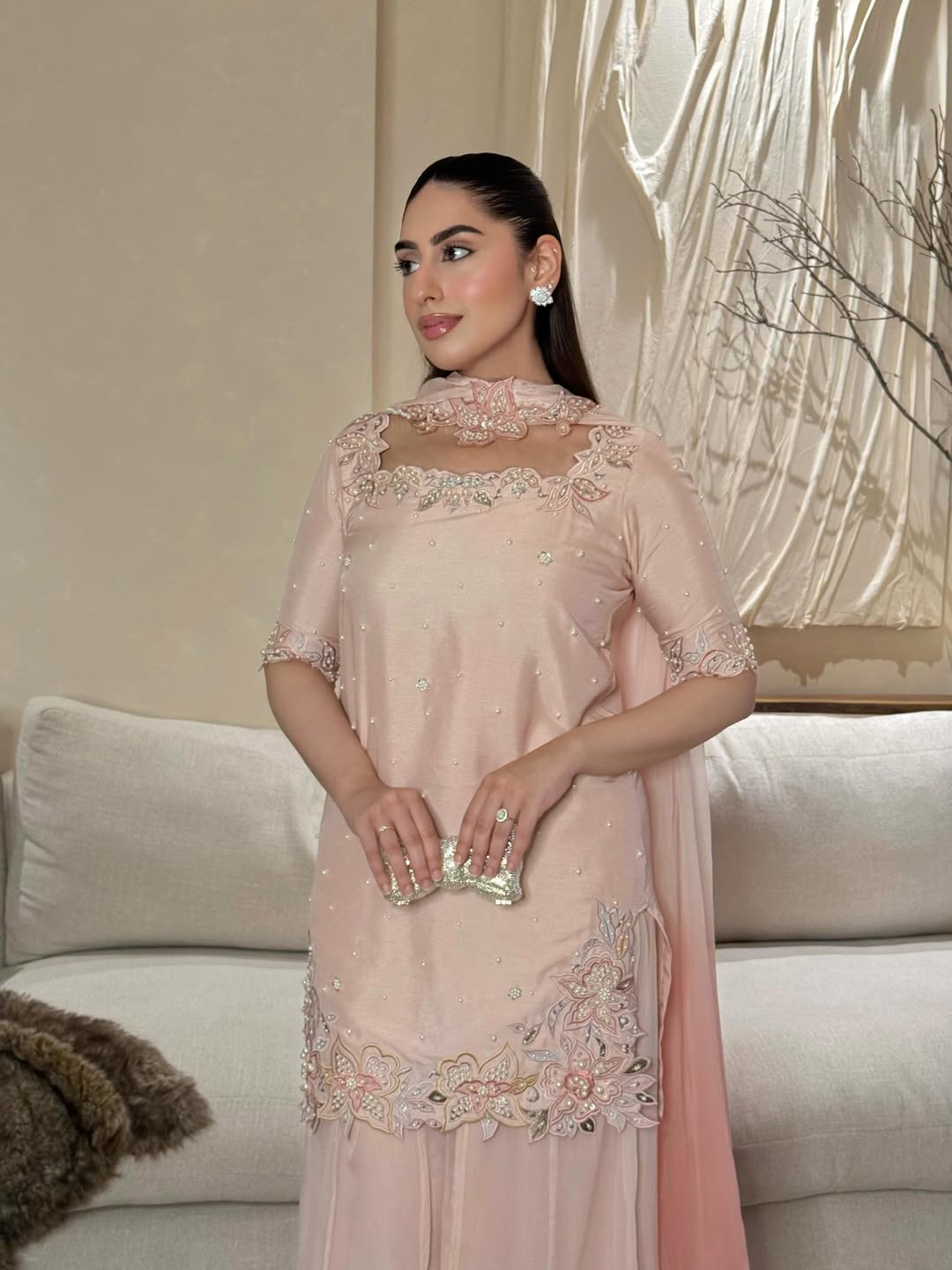 Woman wearing a pink embroidered dress in a living room setting